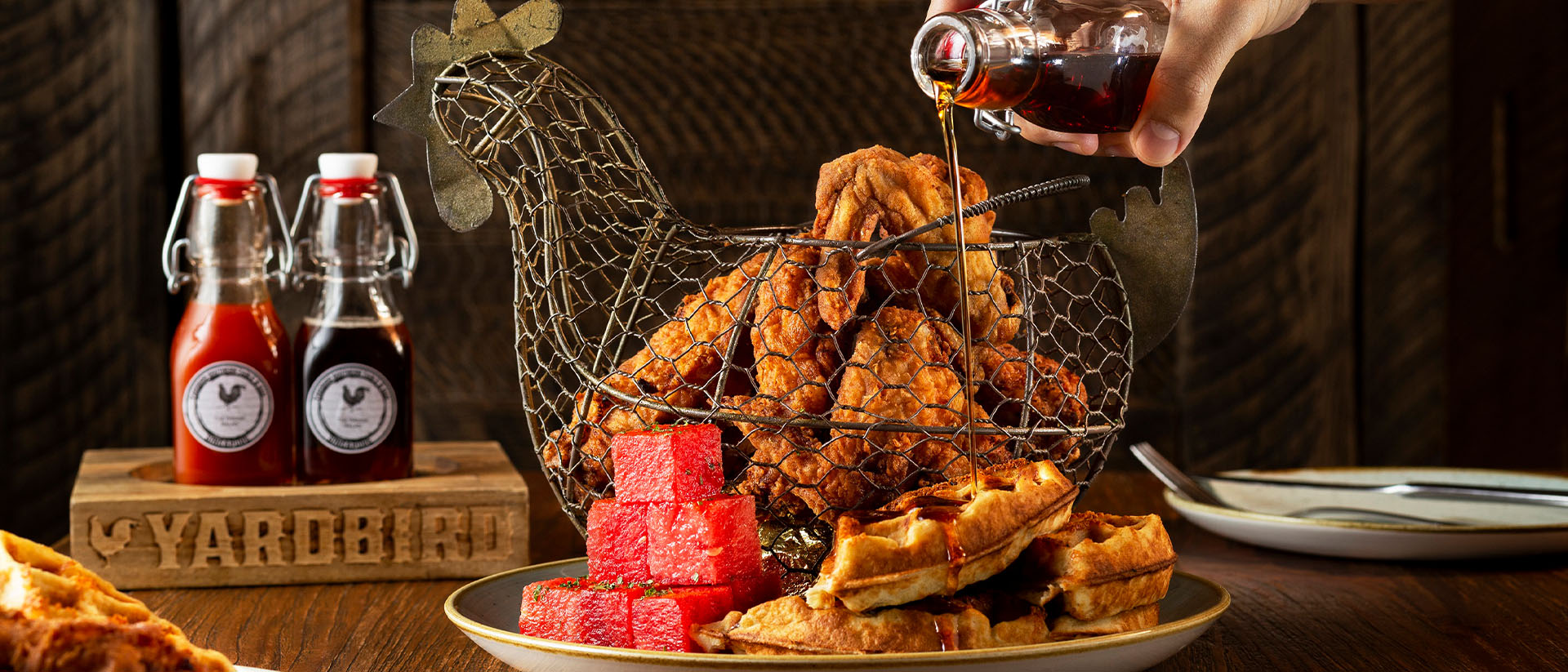 Person poring sauce over fried chicken at Yardbird, the best lunch place in Singapore